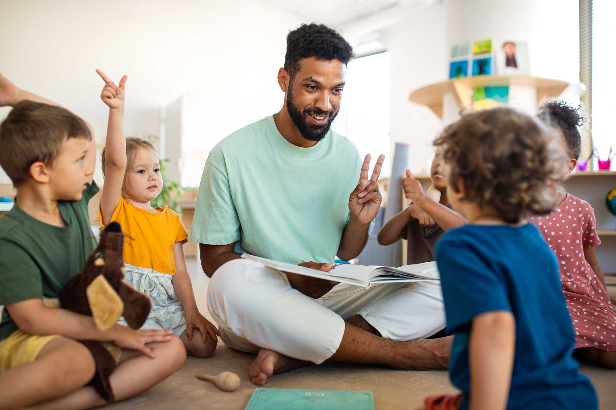 male daycare teacher sitting on the floor doing an activity with a group of students